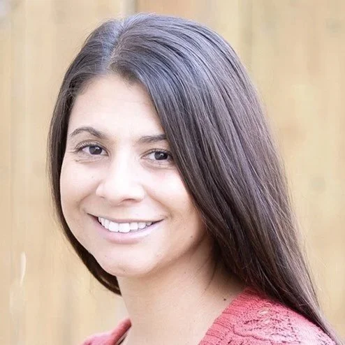 Lindsay Garey, BS - Headshot - A young woman with long, dark hair smiling at the camera against a wooden fence background.