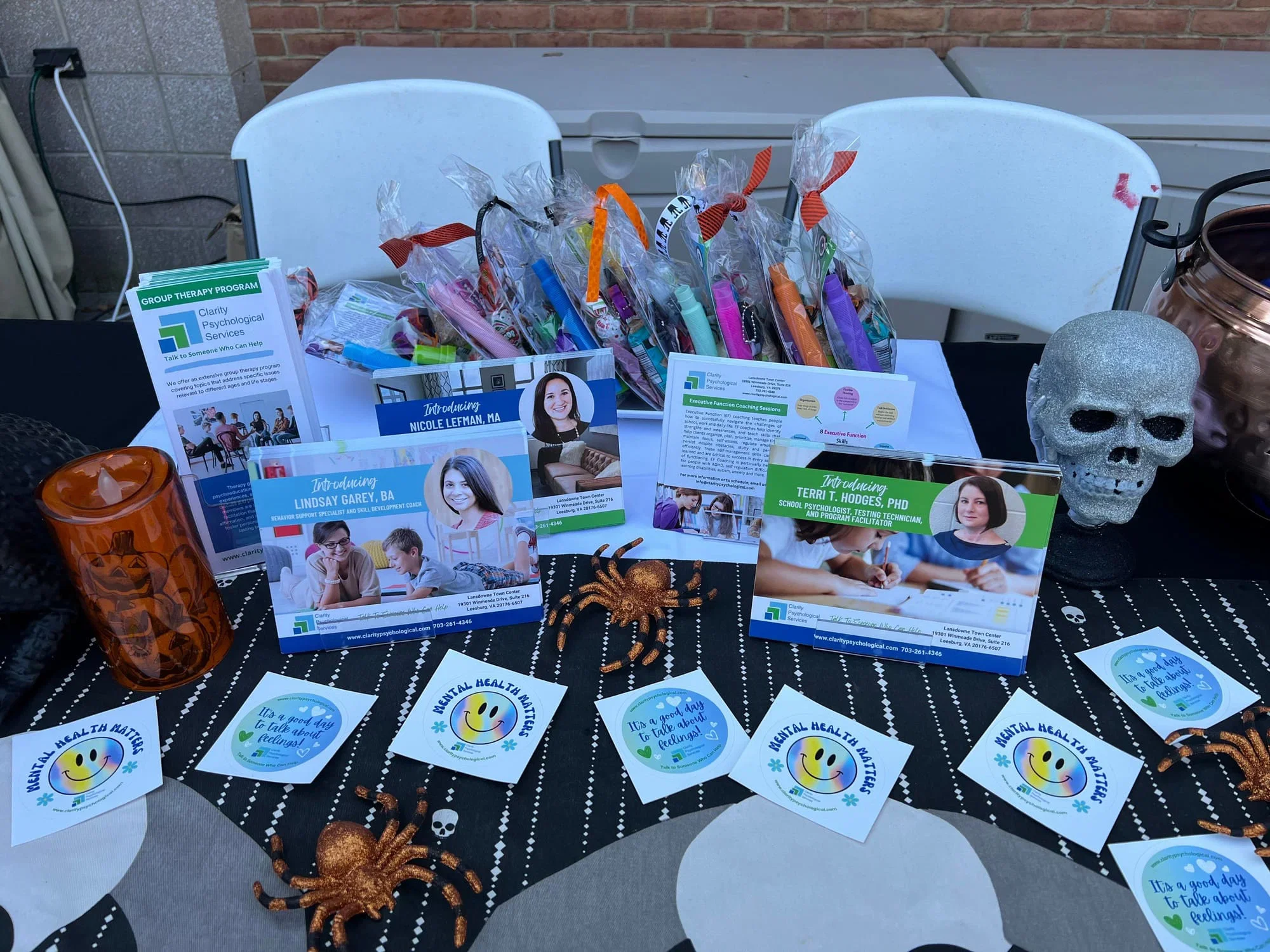 Table set up for a mental health awareness event with brochures, smiley face cards, candy, Halloween-themed decorations, and promotional materials for counseling programs.