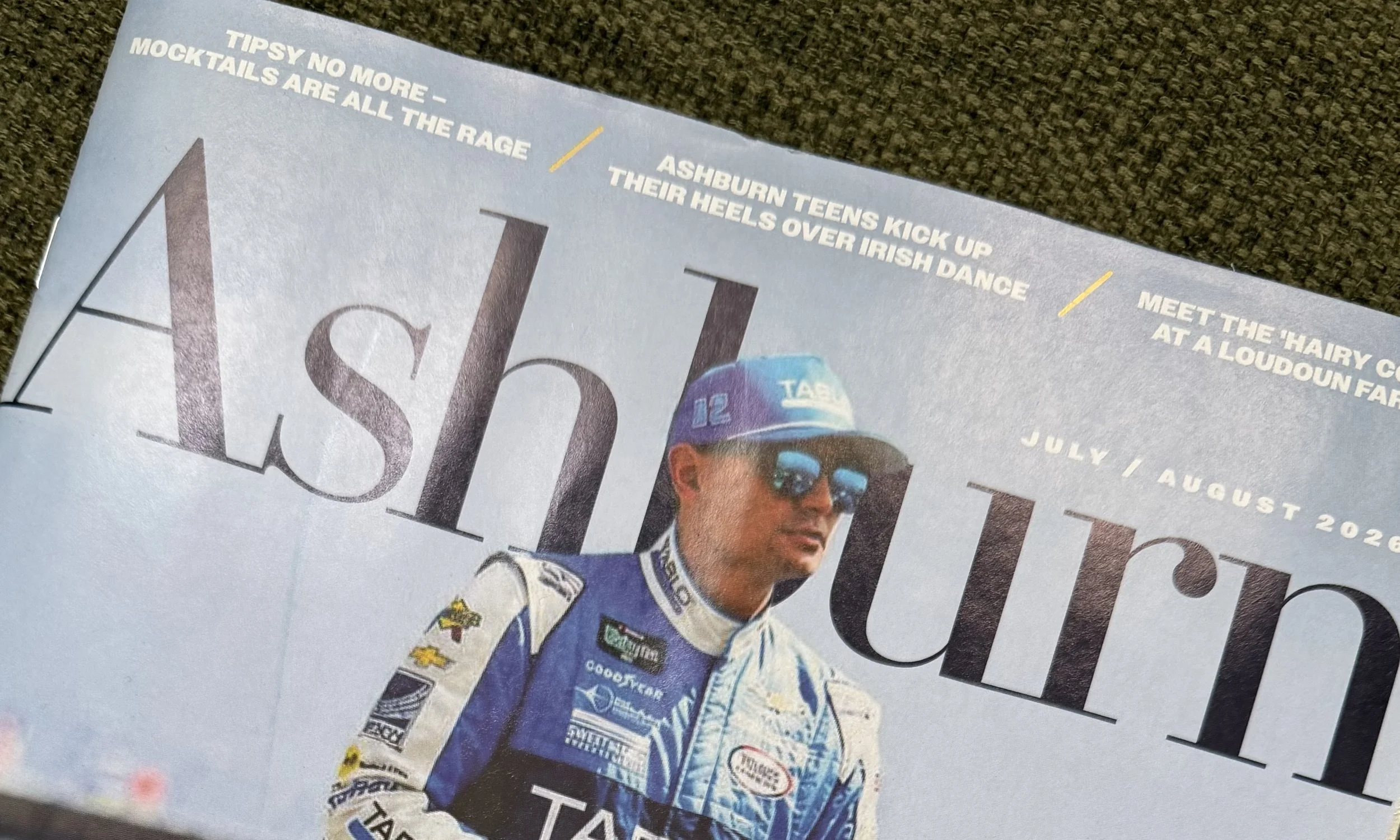 A magazine page featuring a racing driver in a blue and white racing suit and cap, with text about sports events and dates around the image.
