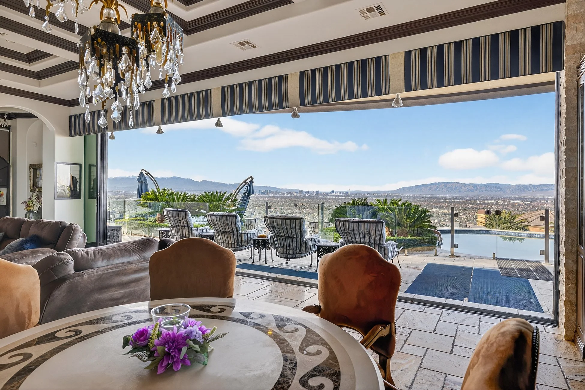 Living room with large open sliding glass doors leading to a balcony with outdoor chairs, overlooking a cityscape and mountains in the distance.