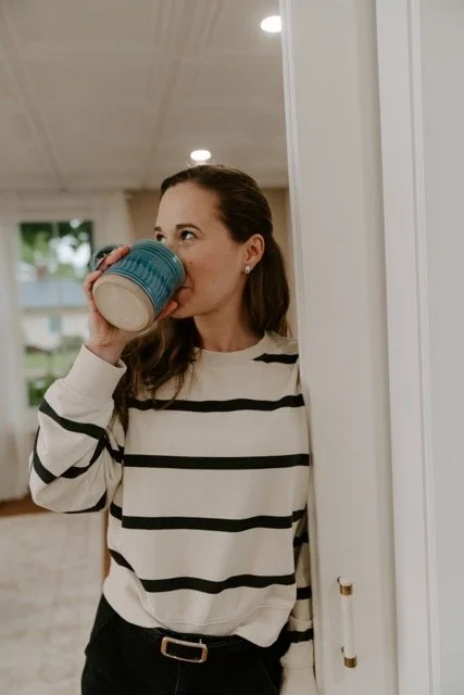 Female therapist with brown hair drinking from a teal mug in an office interior.