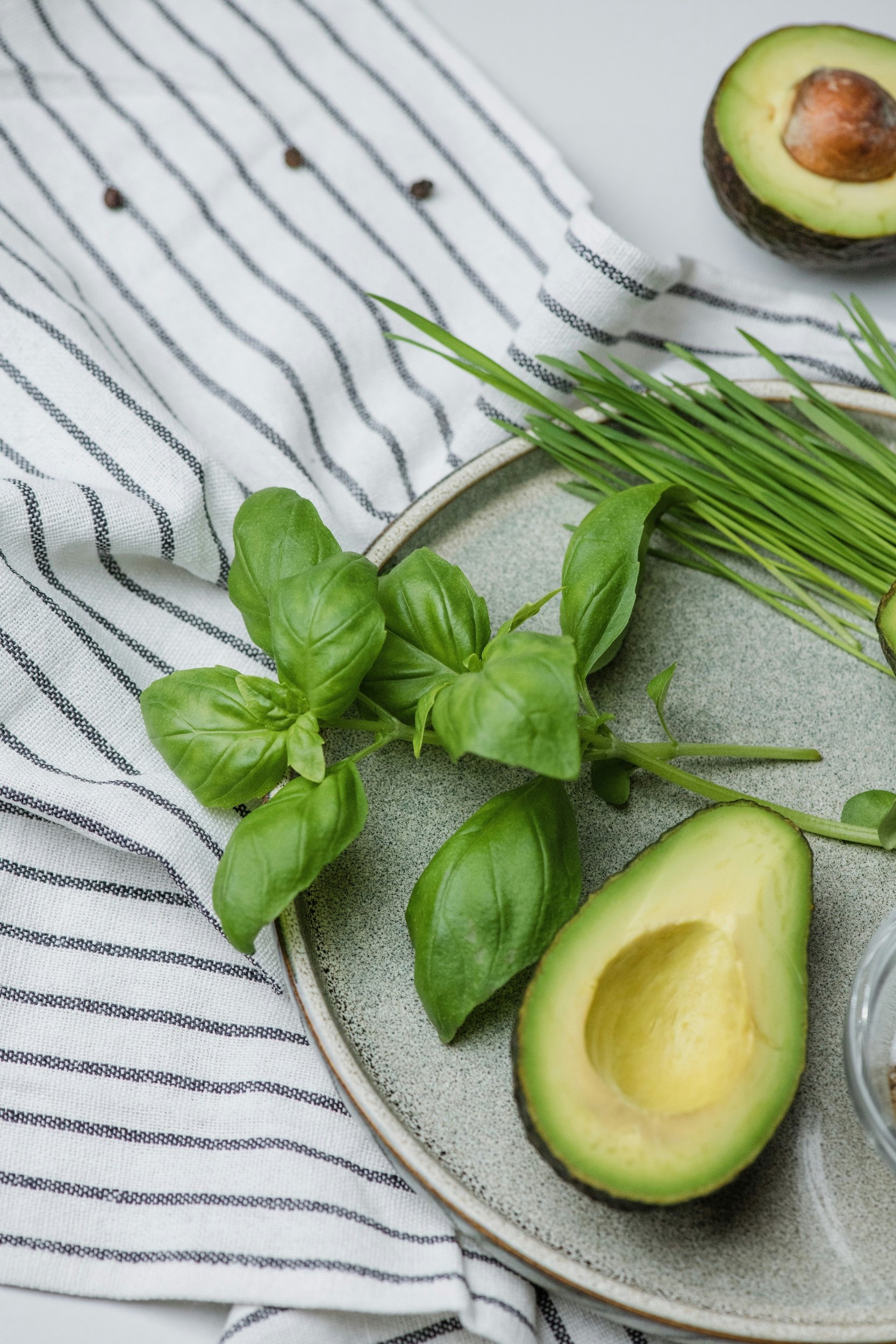 Sliced avocado and fresh basil on a plate with a striped cloth background.