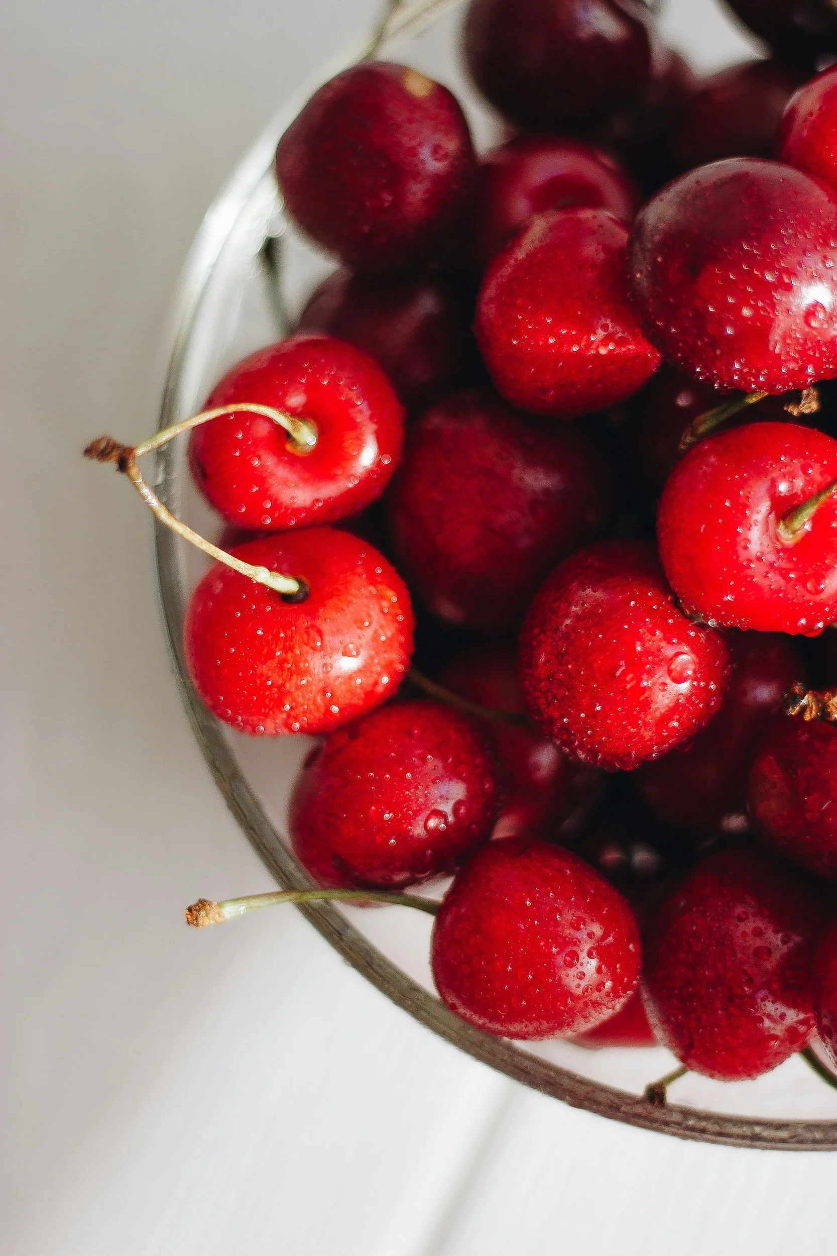 Close-up of fresh red cherries with water droplets in a glass bowl on a light surface.