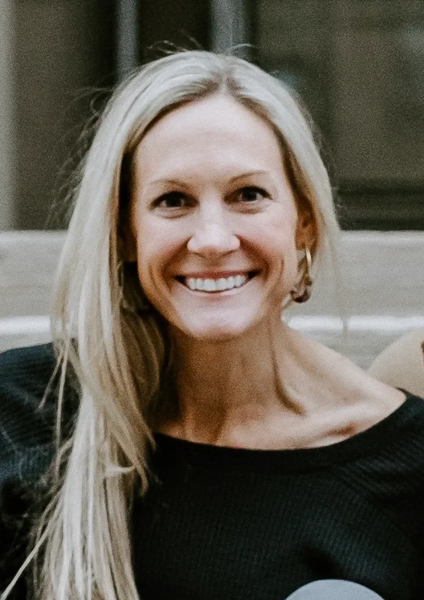 Close-up of a smiling blond woman with long hair wearing a black top.