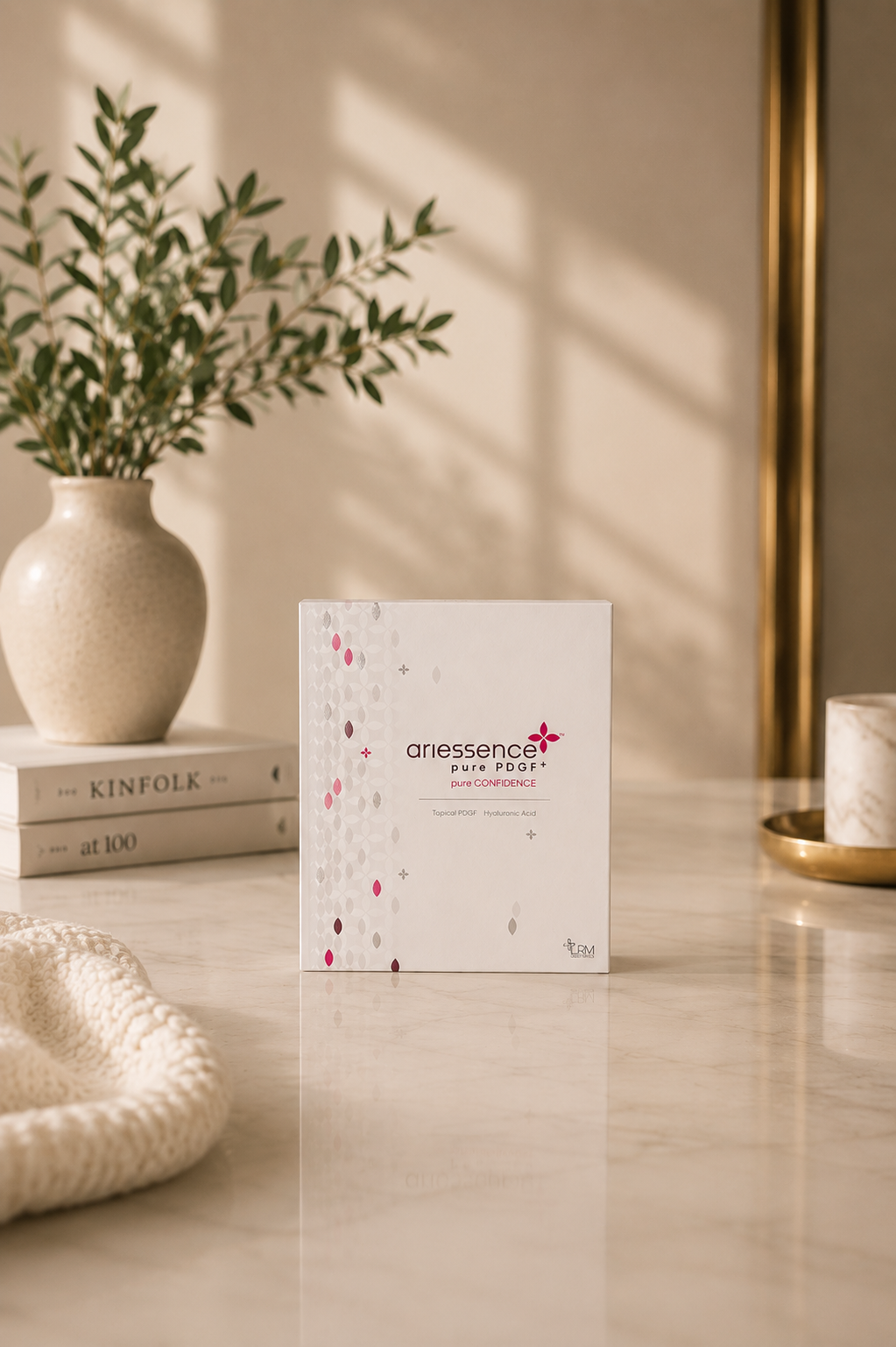 A box of Ariessence pure PDGF+ skincare product on a marble countertop with a potted plant and books in the background, natural light casting shadows.