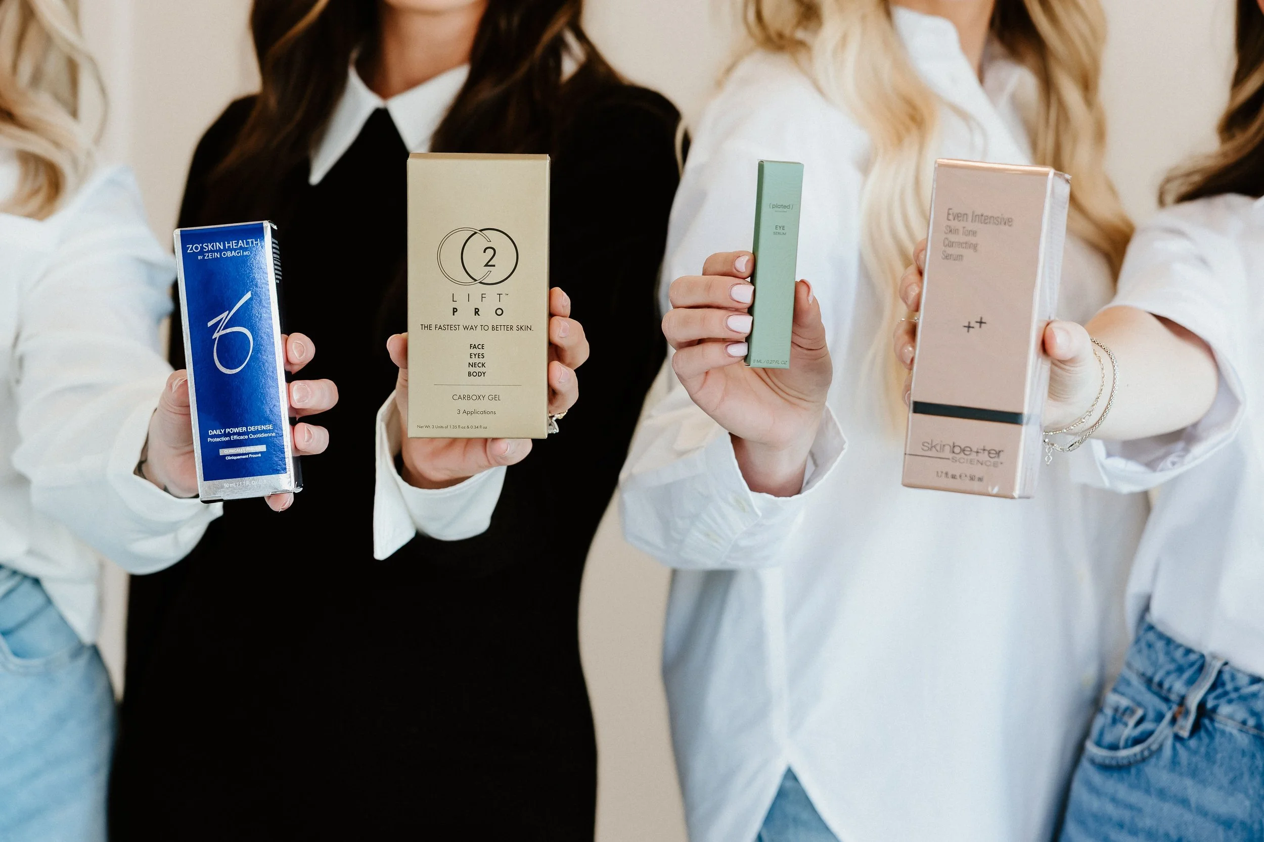 Group of women holding skincare product boxes, including brands like Skinbetter Science, Zel Obagi, and others.