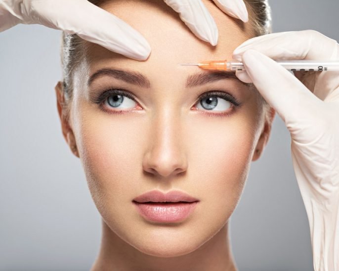 Close-up of a woman receiving a cosmetic injection on her forehead by a person wearing gloves.