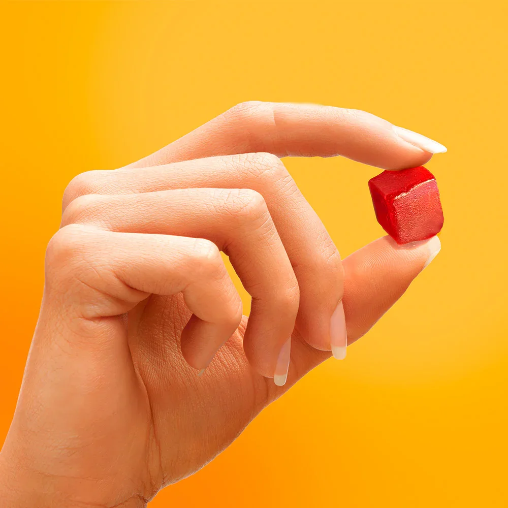 Close-up of a hand holding a small red cube against a yellow-orange background.