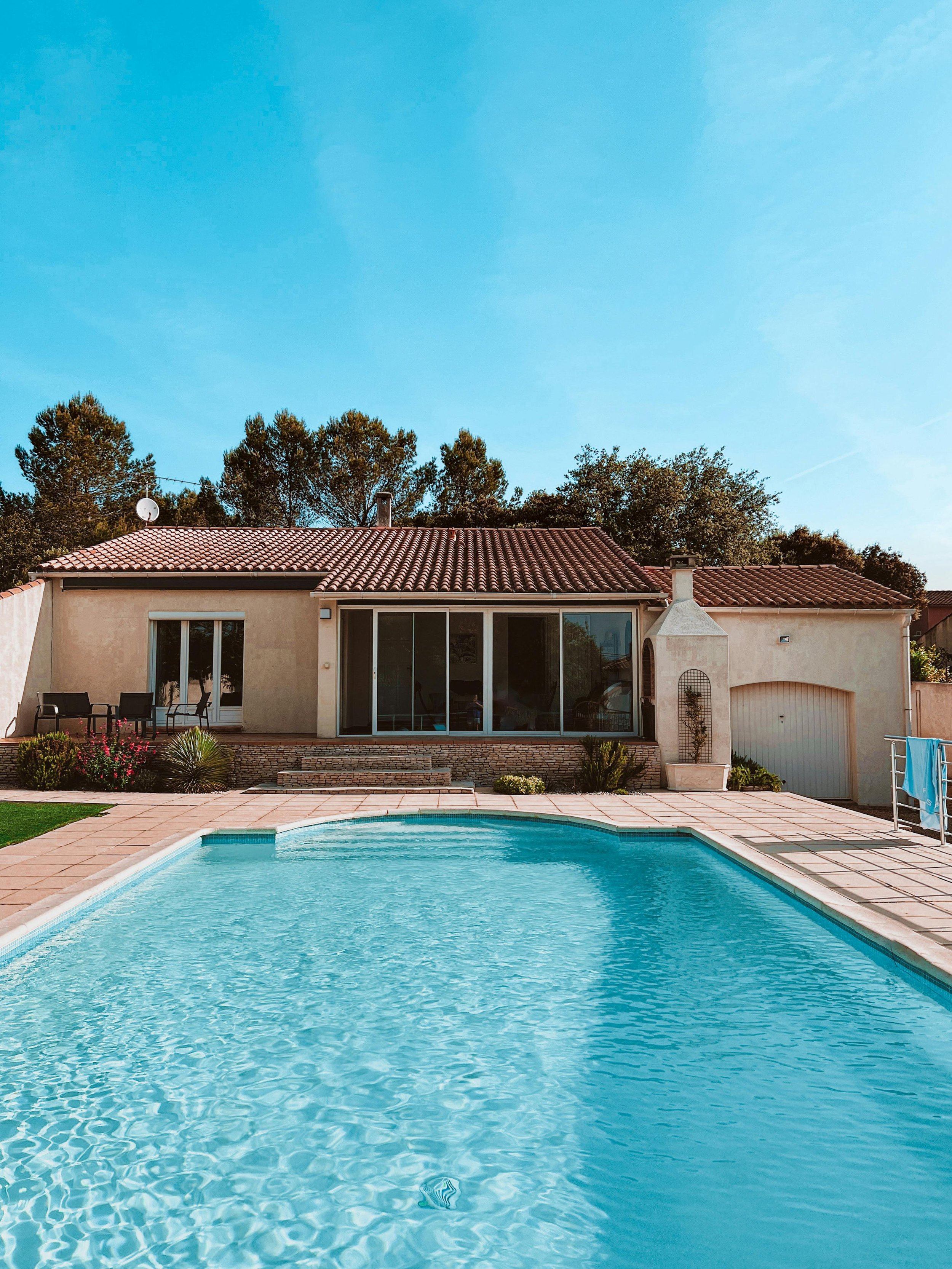 Backyard with swimming pool, house with beige exterior, patio furniture, and clear blue sky.