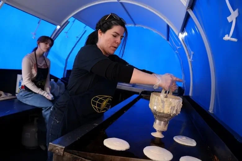 Woman inside a tent uses a device to pour pancake batter on a griddle.
