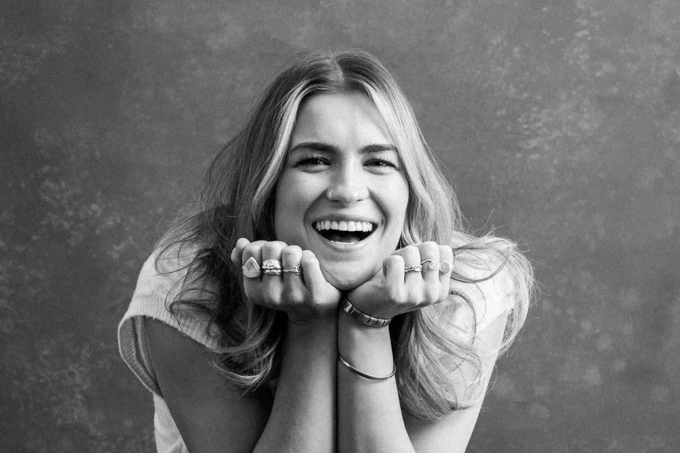 close up black and white photo of girl smiling with her chin in hands