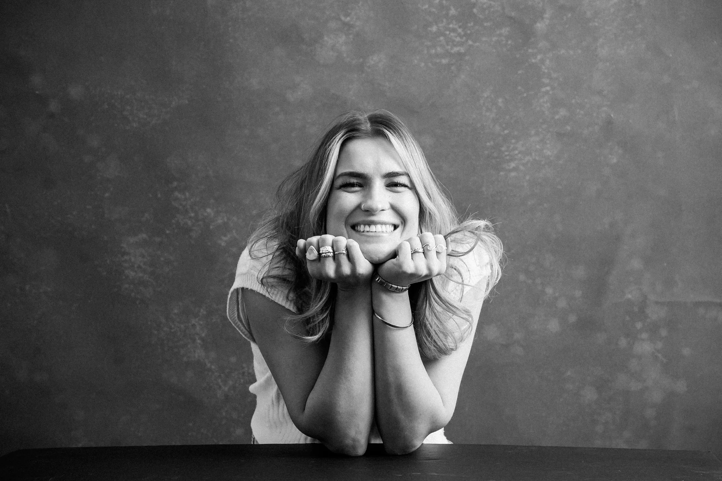 black and white picture of girl smiling with her elbows resting on a table with her chin on her hands