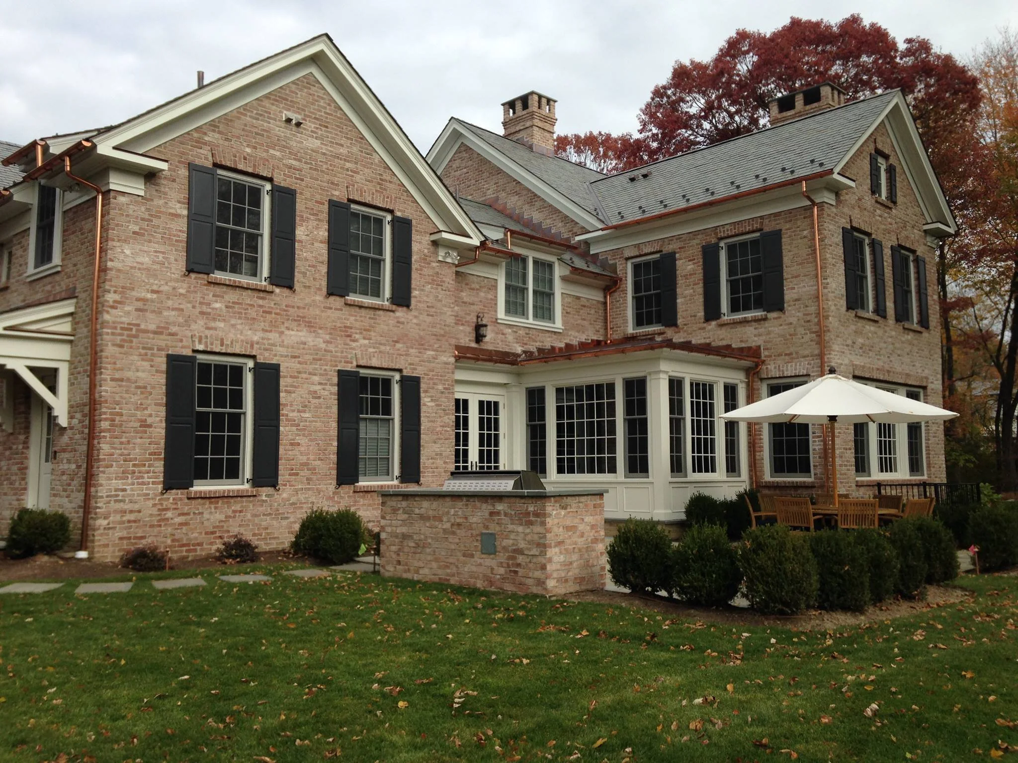 Brick house with black shutters, white trim, and a patio with a white umbrella and outdoor furniture.