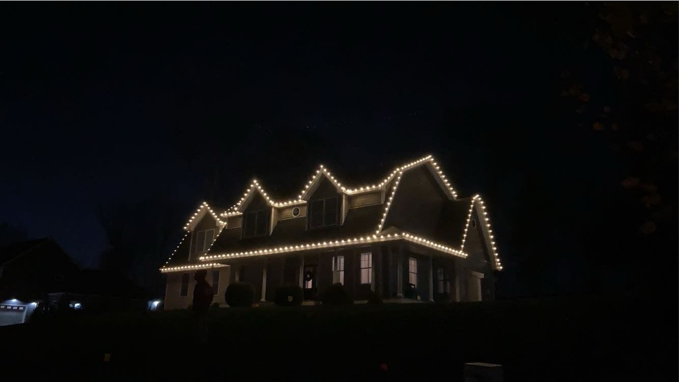 A large house decorated with string lights outlining its roof and windows at night.
