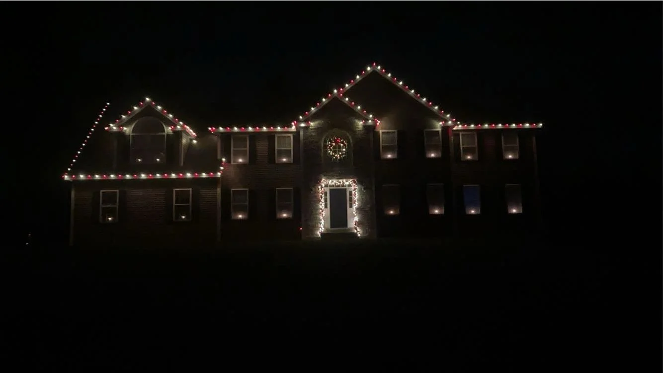 A large house decorated with Christmas string lights outlining the roof and windows at night.