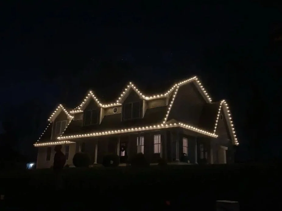A large house decorated with string lights outlining the roof and windows at night.
