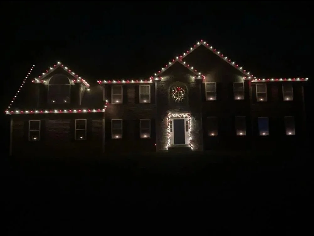 A large house decorated with Christmas string lights outlining the roof and windows at night.