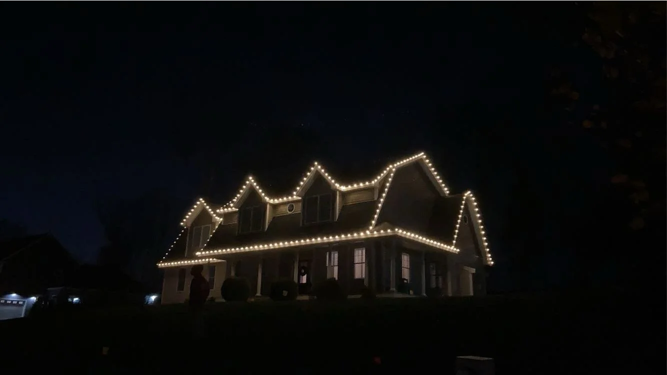 A large house decorated with string lights outlining the roof and windows at night.