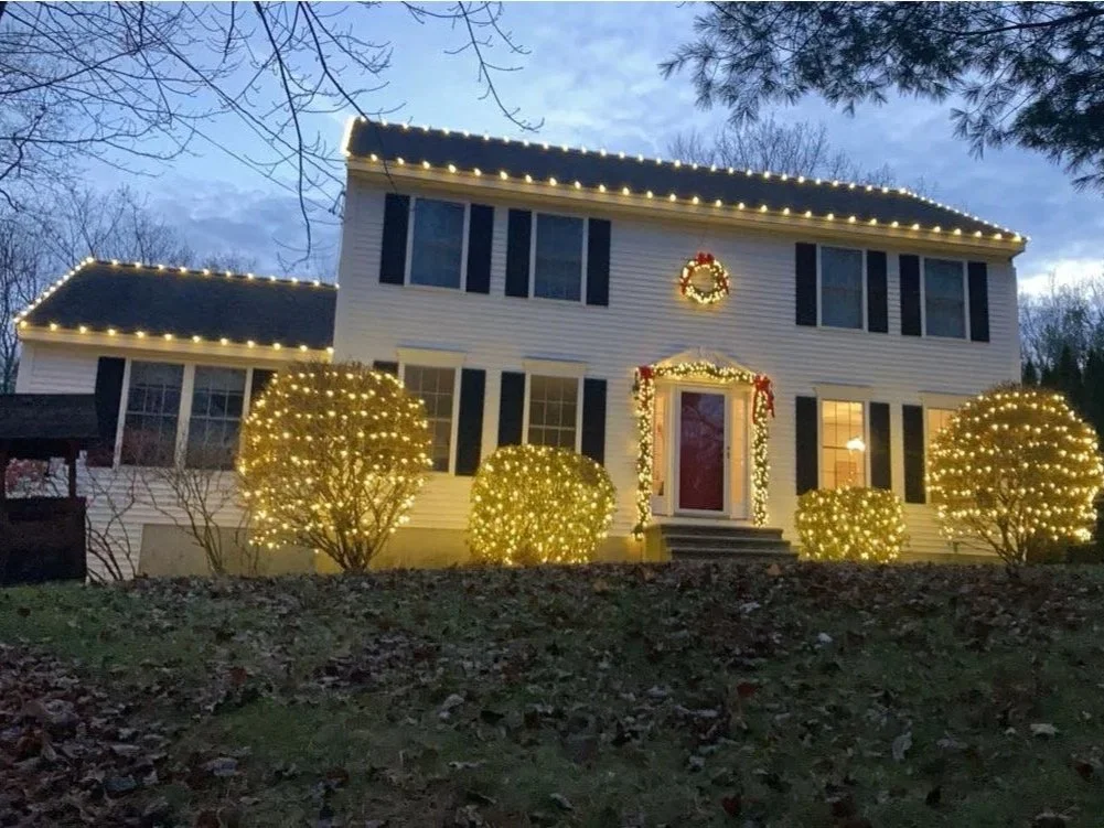 A two-story house decorated with Christmas lights, wreath, and garlands at dusk.