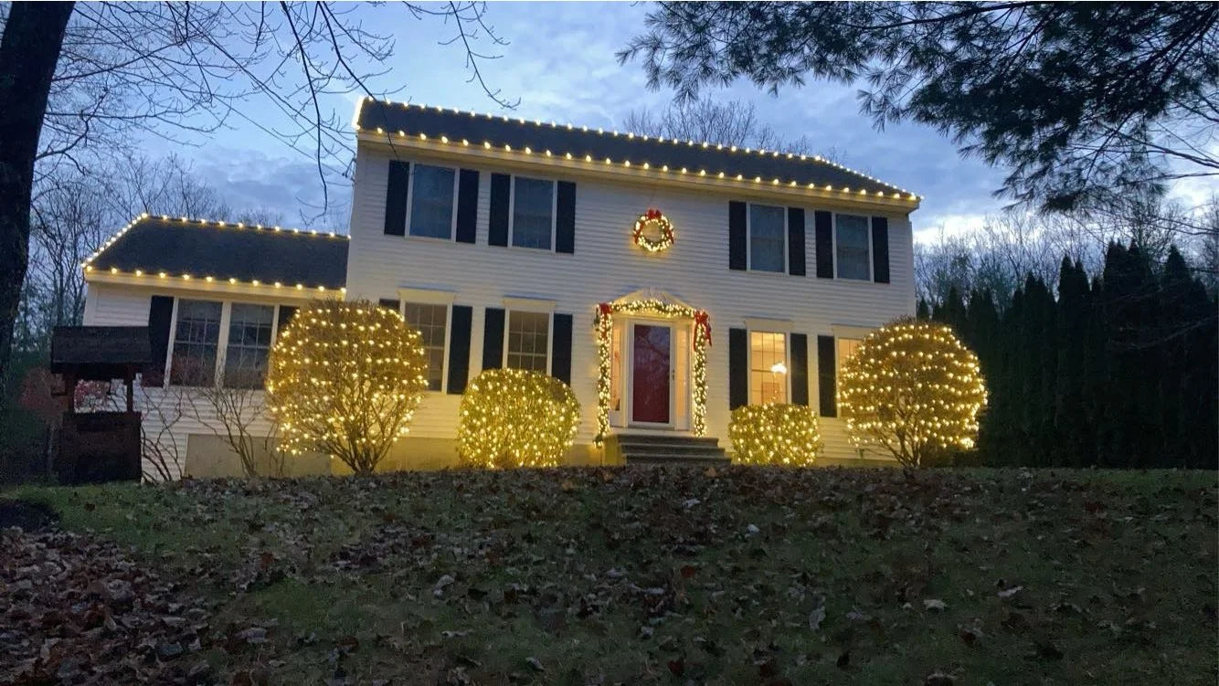 A two-story house decorated with Christmas lights, wreath, and garlands at dusk.