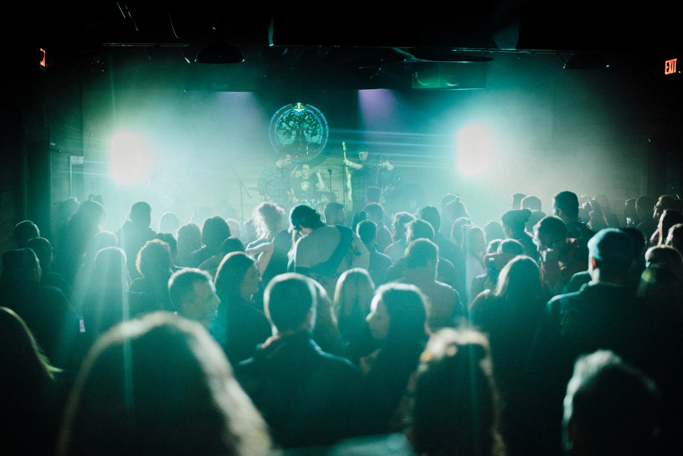 Audience watching a band perform on stage with bright lights in a dark venue.