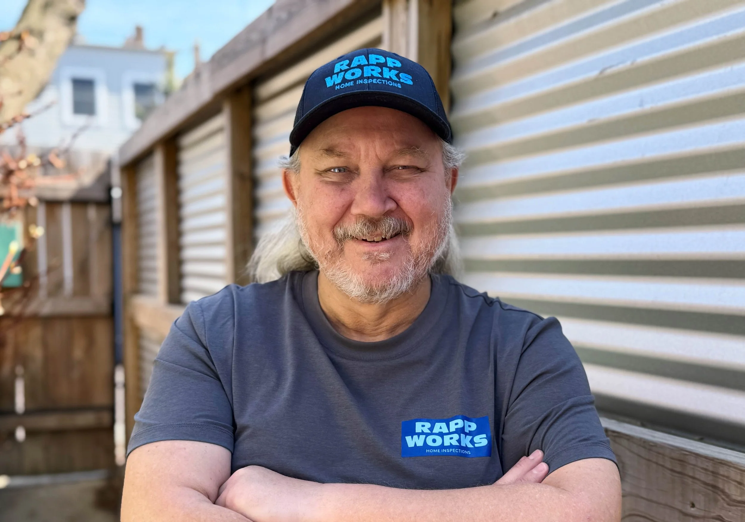 Home Inspection, Chicago, Illinois, Michigan blue logo that says "RAPP WORKS Home Inspections", standing outdoors against a wooden fence and a metal siding wall, with suburban houses in the background.