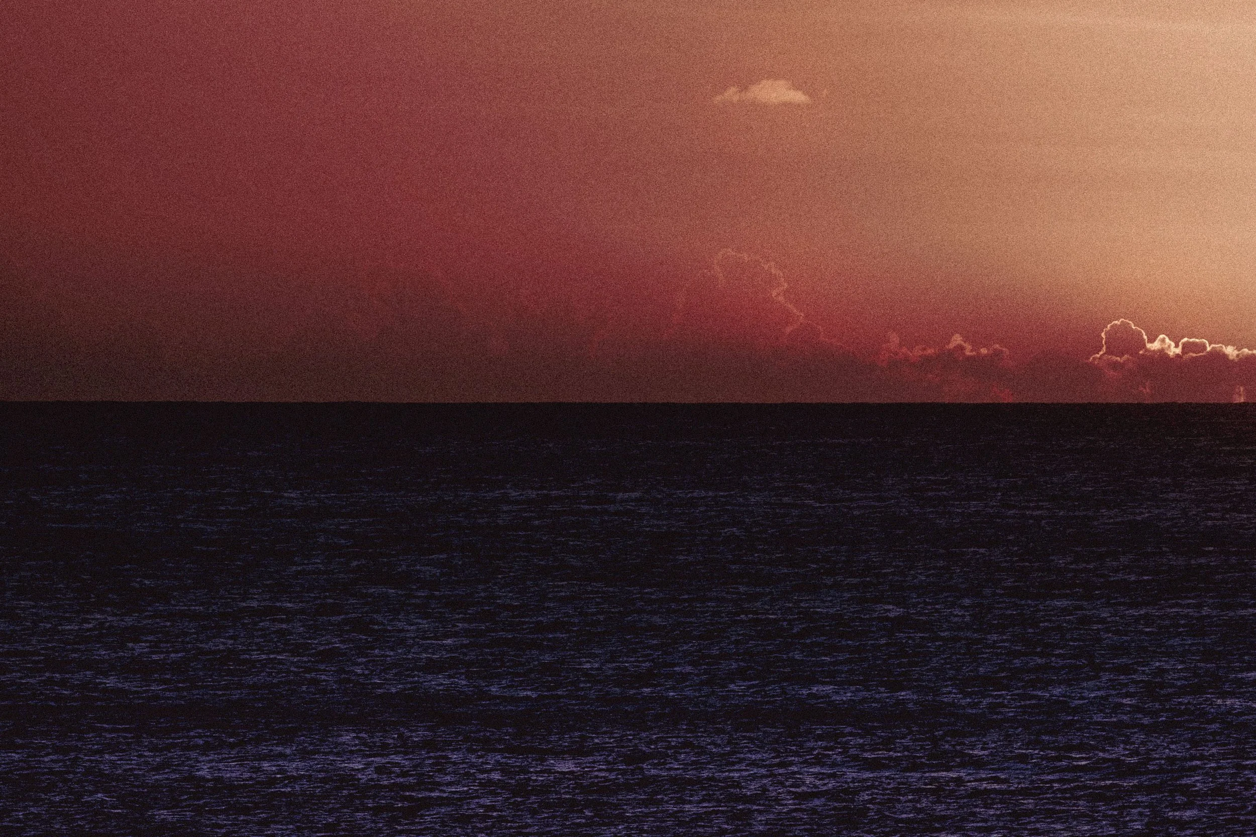 Ocean under a reddish-orange sunset with scattered clouds.