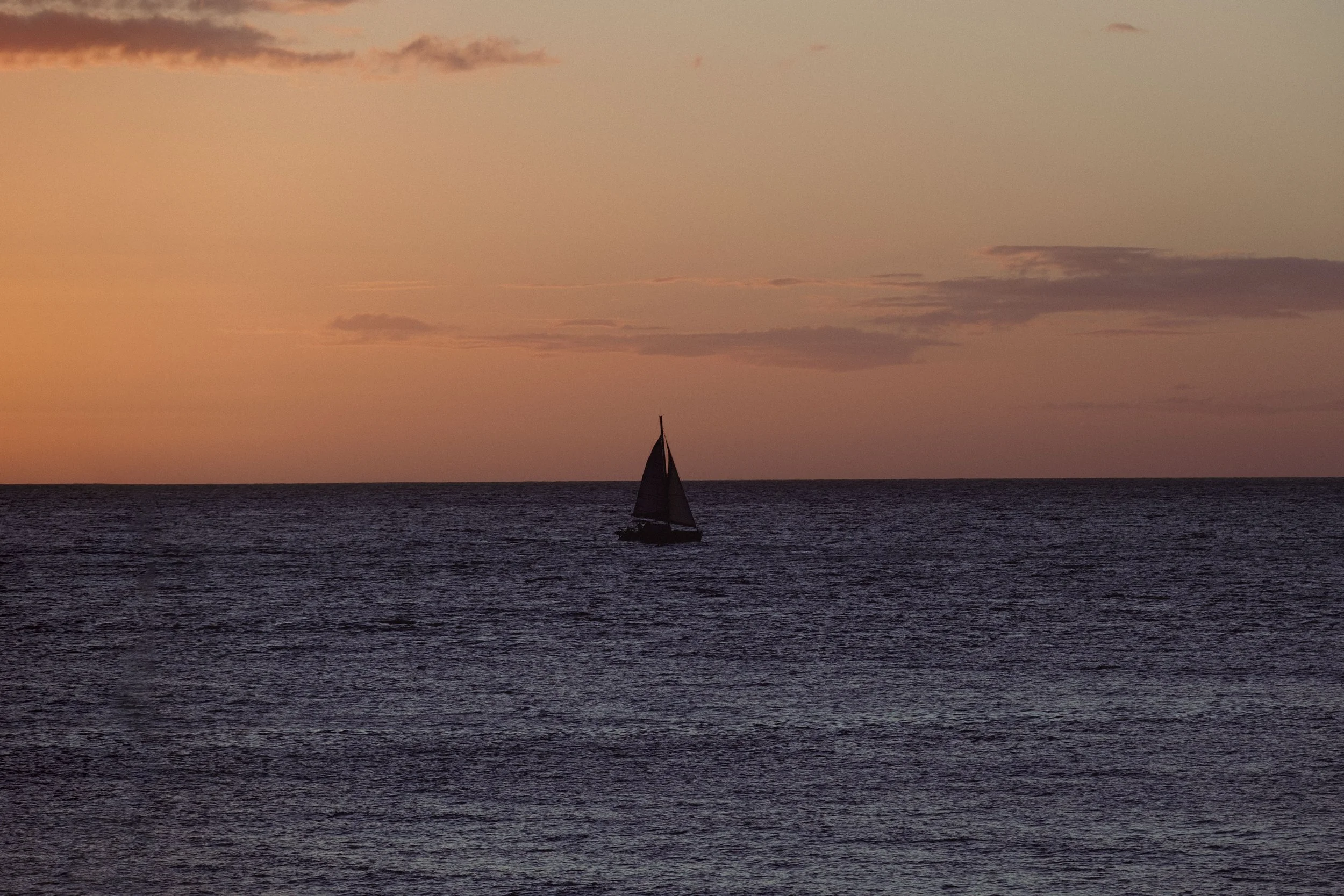 A sailboat on the water during sunset with a pink and orange sky and some clouds.