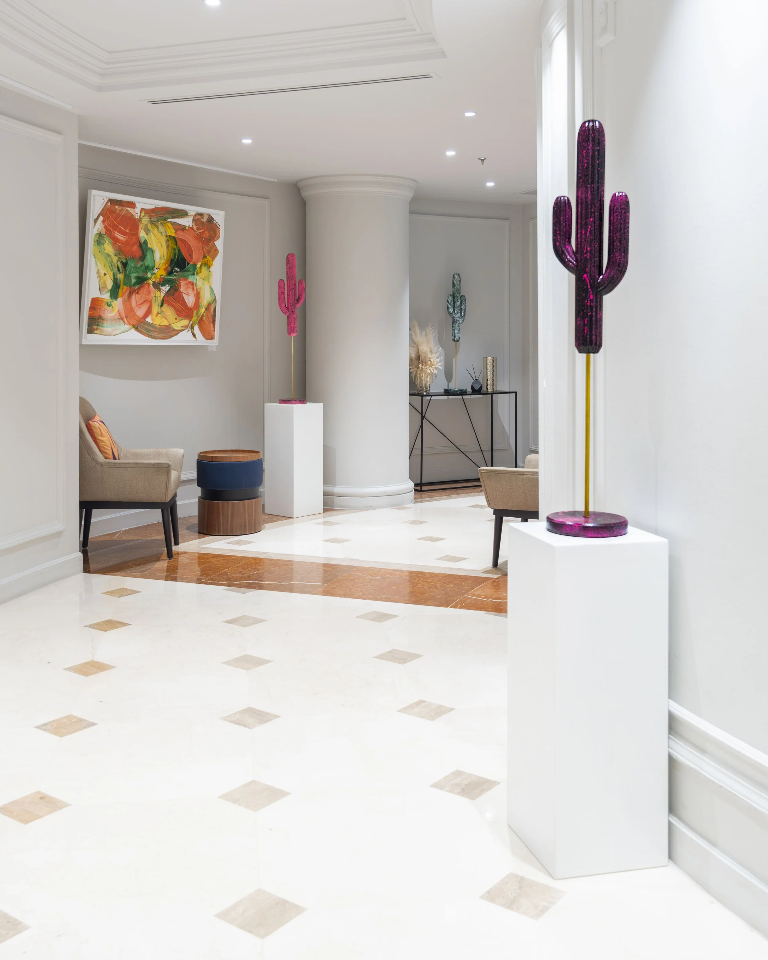 Interior view of a modern building lobby with white walls and flooring, decorated with colorful cactus sculptures and abstract artwork.