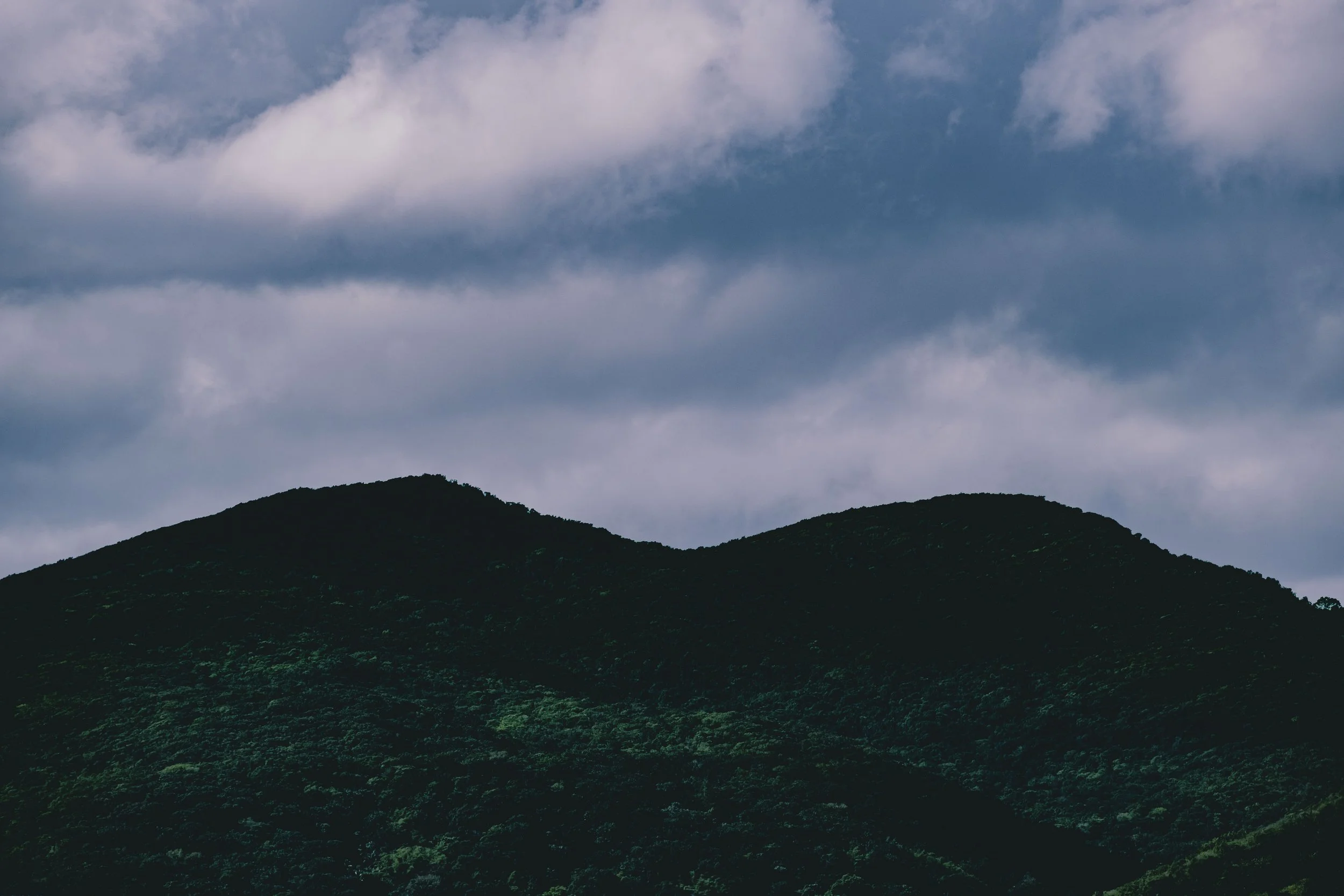 Green mountain range under cloudy sky.