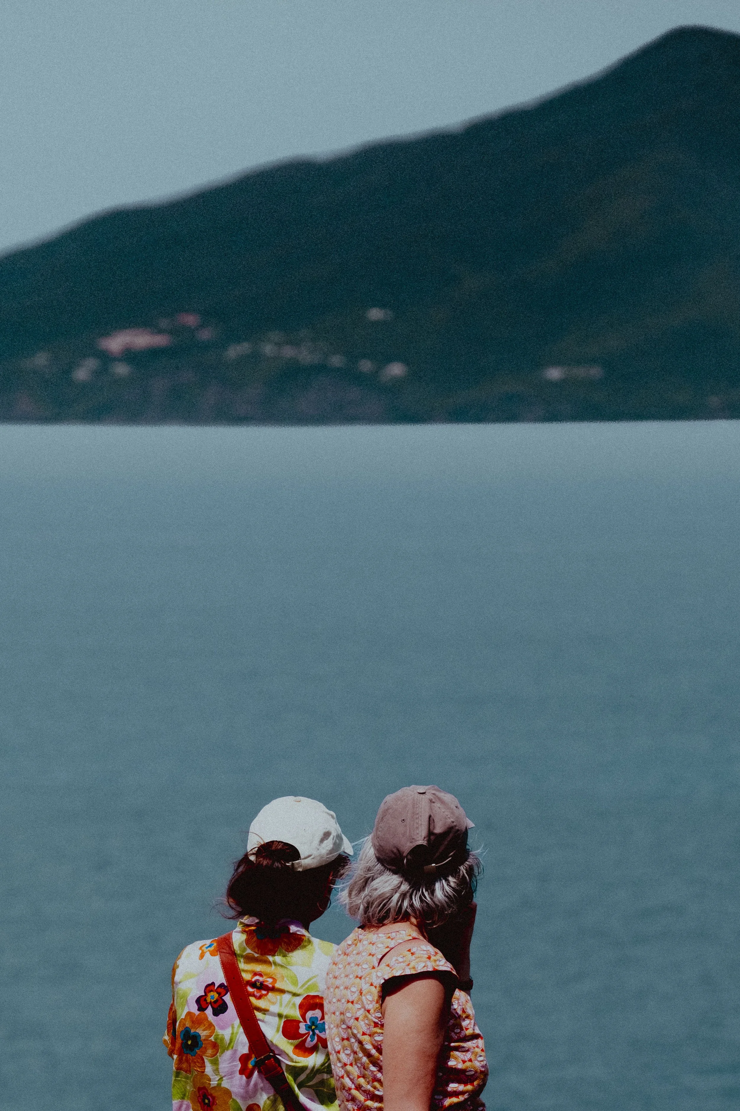 Two elderly women with hats looking at a large body of water with a mountain in the background.