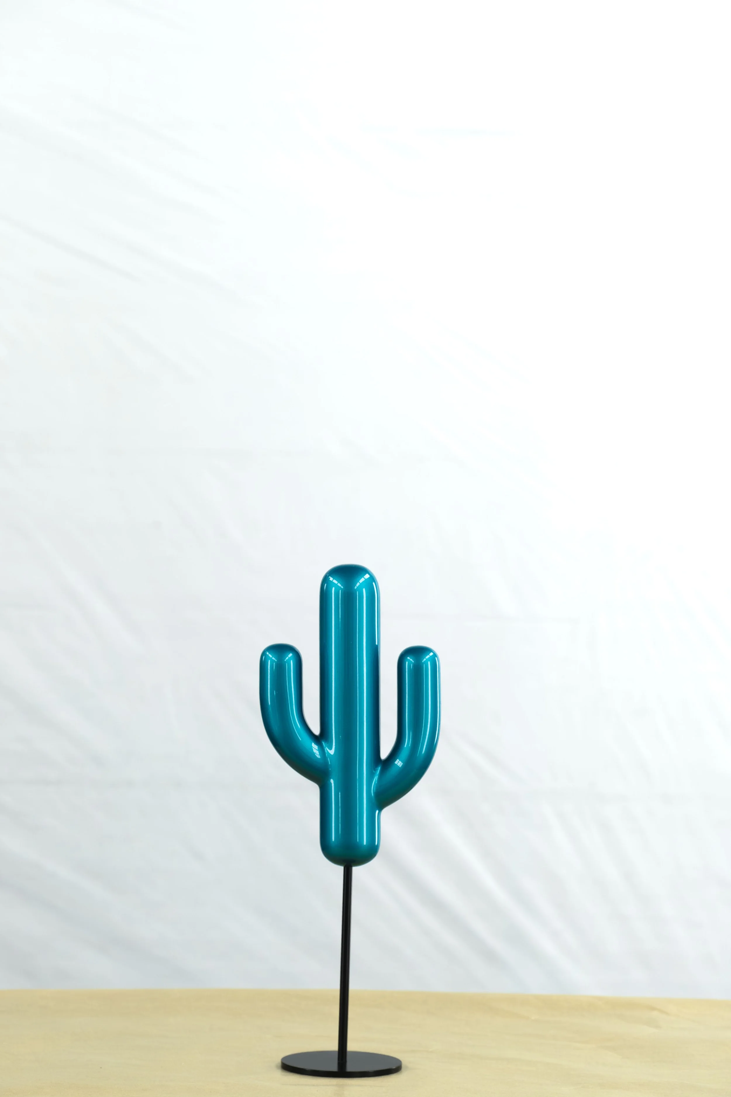 Blue cactus-shaped balloon sculpture on a black stand on a wooden surface.