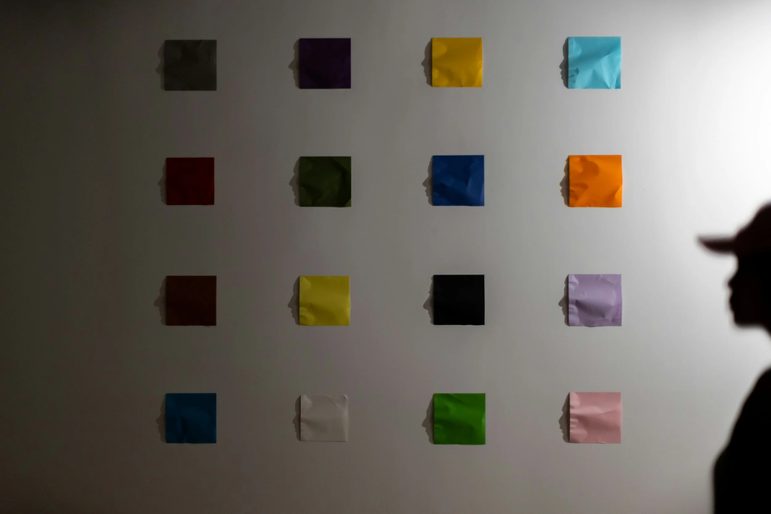 A wall with twenty colored sticky notes arranged in four rows. The colors include black, purple, yellow, blue, red, green, orange, brown, white, and pink.