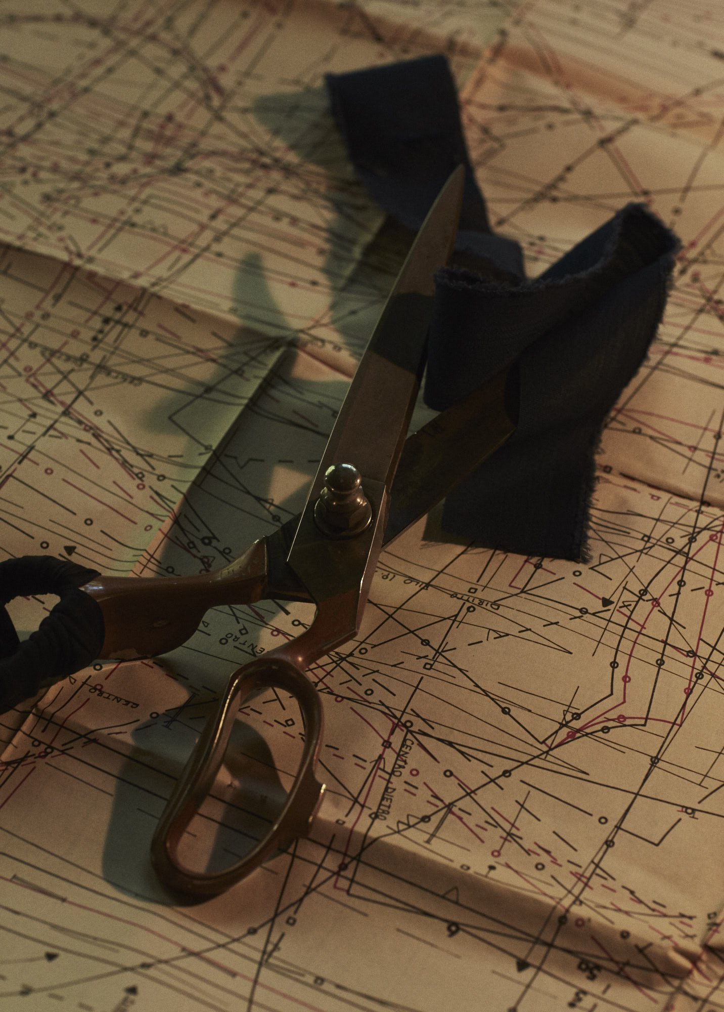 A pair of scissors with a black handle and metallic blade lying on a musical score or sheet music with a black ribbon or strip of fabric nearby.