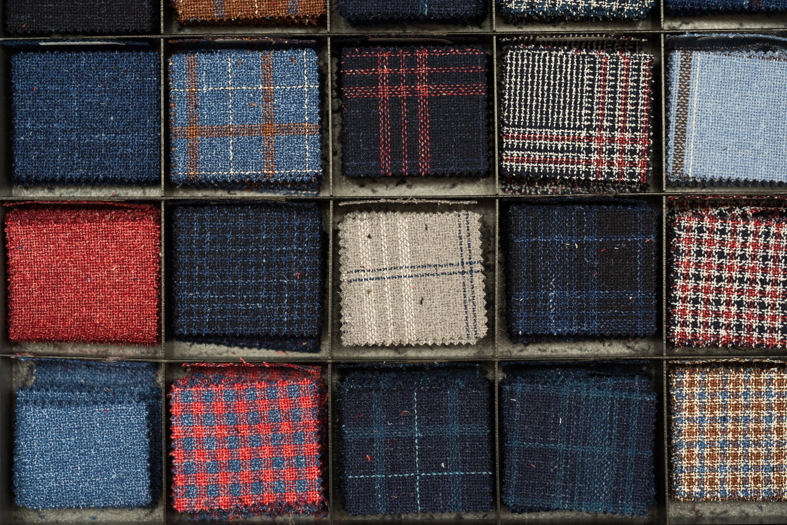 A collection of folded fabric swatches with various plaid and checkered patterns in shades of blue, red, black, white, gray, and brown, stored in designated compartments.