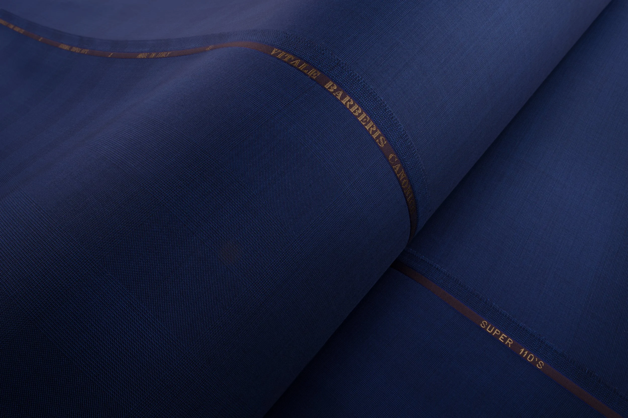 Close-up of dark blue fabric with gold text, showing a roll of fabric material.