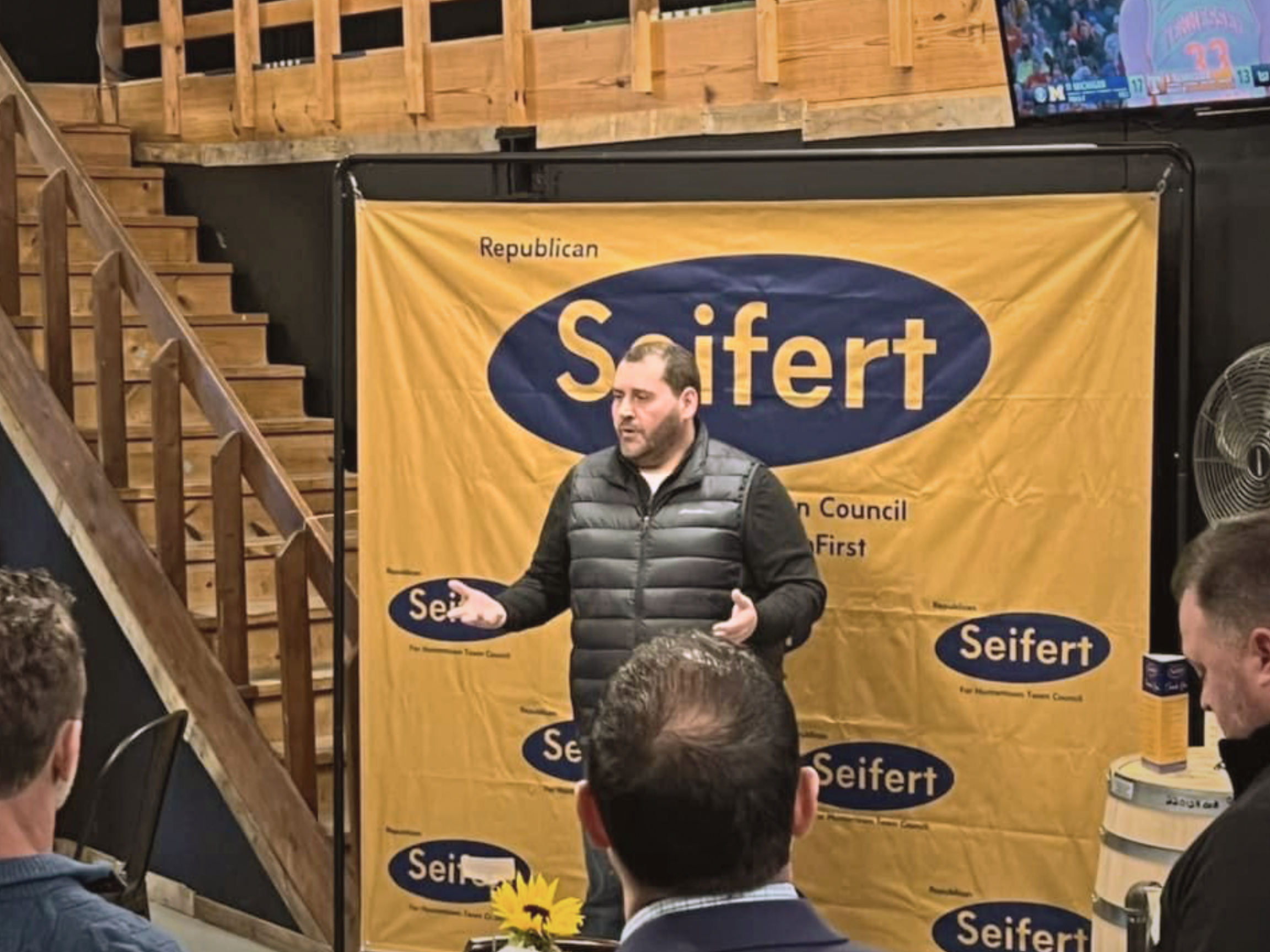 A man named Brandon Seifert speaking to an audience in front of a yellow Seifert campaign banner with the words 'Republican', 'Seifert'.