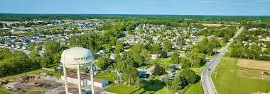 Aerial view of a suburban Huntertown, Indiana area with houses, streets, trees, and a water tower, with a clear blue sky.