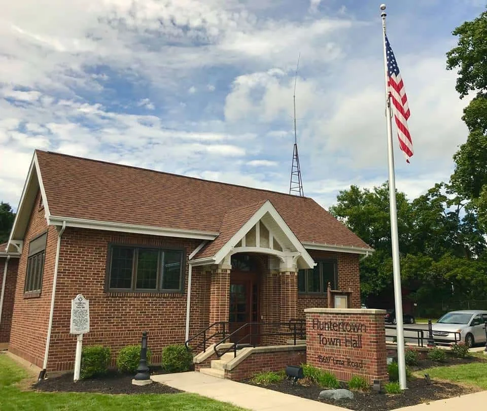 A brick building labeled 'Duluth Town Hall' with an American flag and a flagpole in front, surrounded by trees and a parking lot.