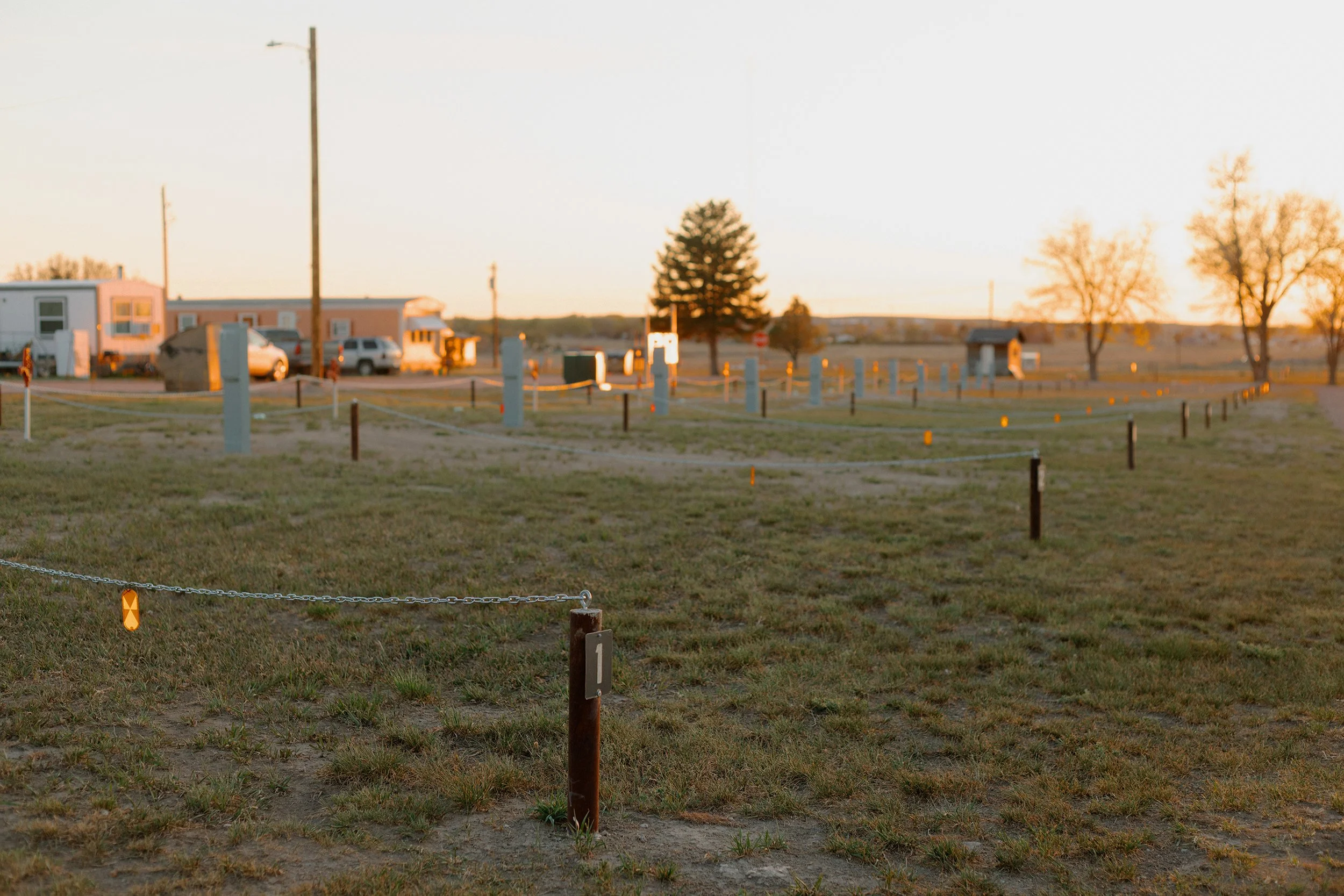 RV pull through campground area during sunset with recreational vehicles, a large pine tree, a few smaller trees, full utility hookup