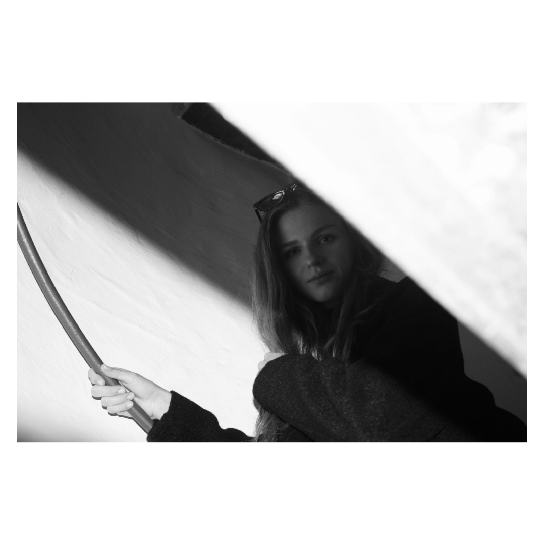 Schwarz-weiß-Foto einer jungen Frau, die einen Regenschirm hält, durch eine Lücke fotografiert.