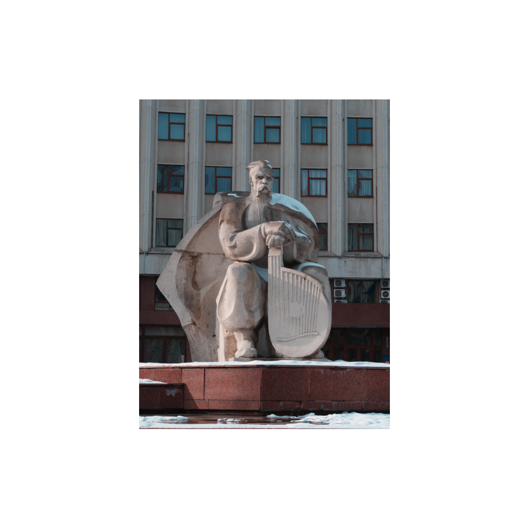 Steinmetzskulptur eines Mannes mit einem Lyra-Instrument, vor einem Mehrfamilienhaus.