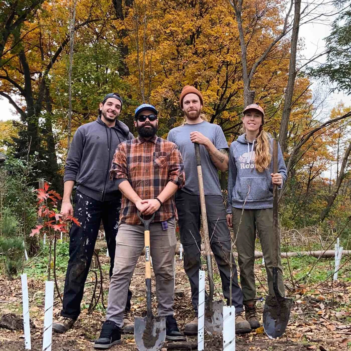 Five people outdoors in a garden or park during fall, holding shovels and posing for a photo.