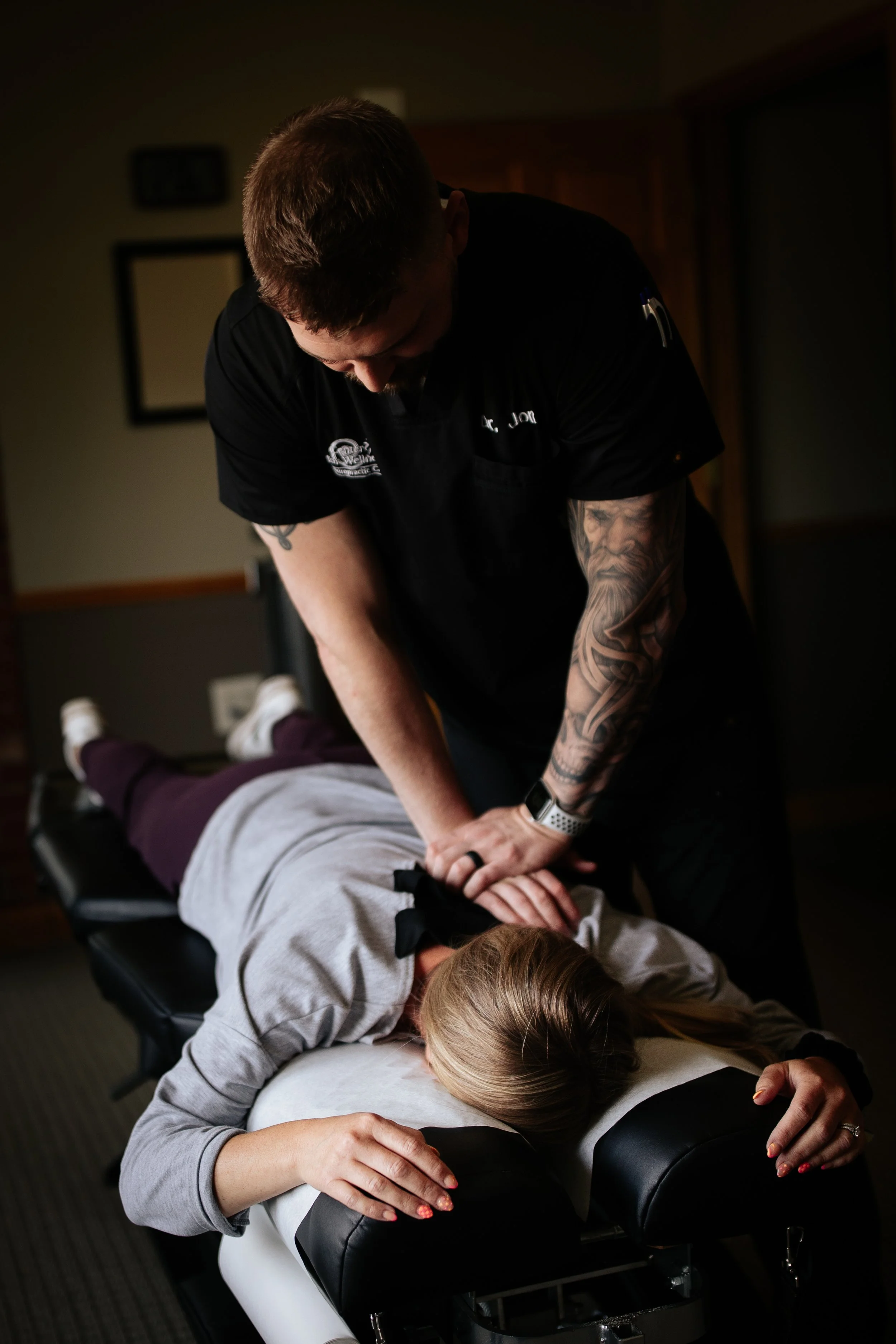 A chiropractor performing an adjustment on a woman lying face down on a chiropractic table.