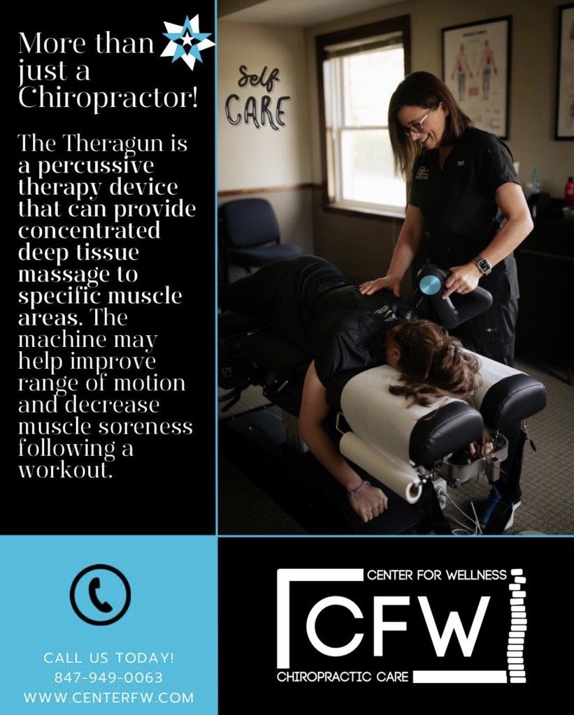 A woman receiving a chiropractic treatment with a TheraGun device while lying face down on a treatment table in a wellness office. The office has posters on the wall, a window, and a sign that reads 'Self Care.'