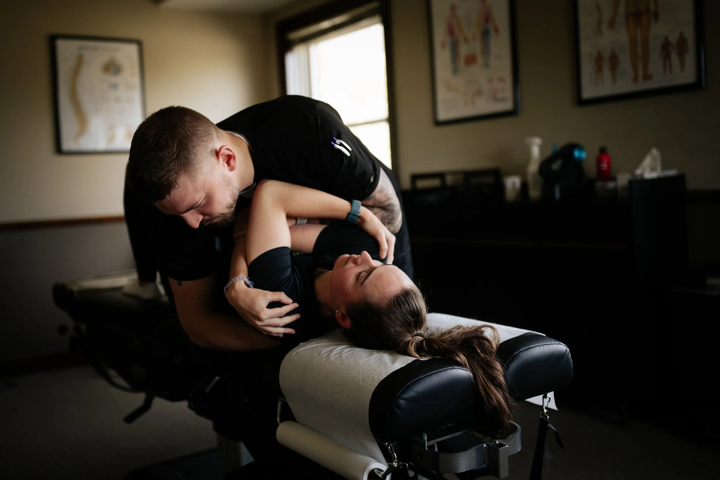 A chiropractor or physical therapist adjusting a woman's neck on an examination table in a clinic or office.