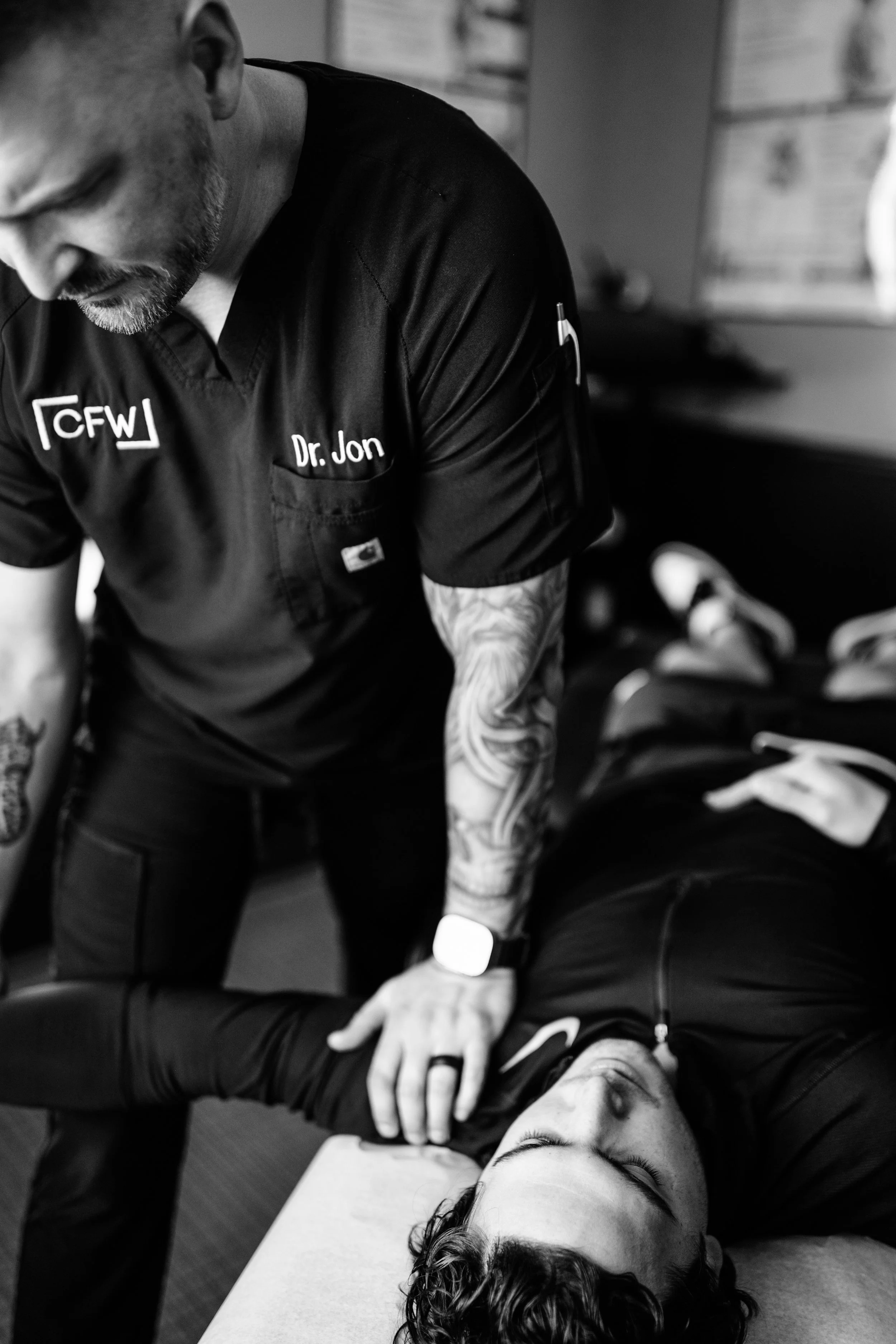 A chiropractor performing an adjustment on a young man's neck while the patient lies on a treatment table with his eyes closed in a clinical setting.