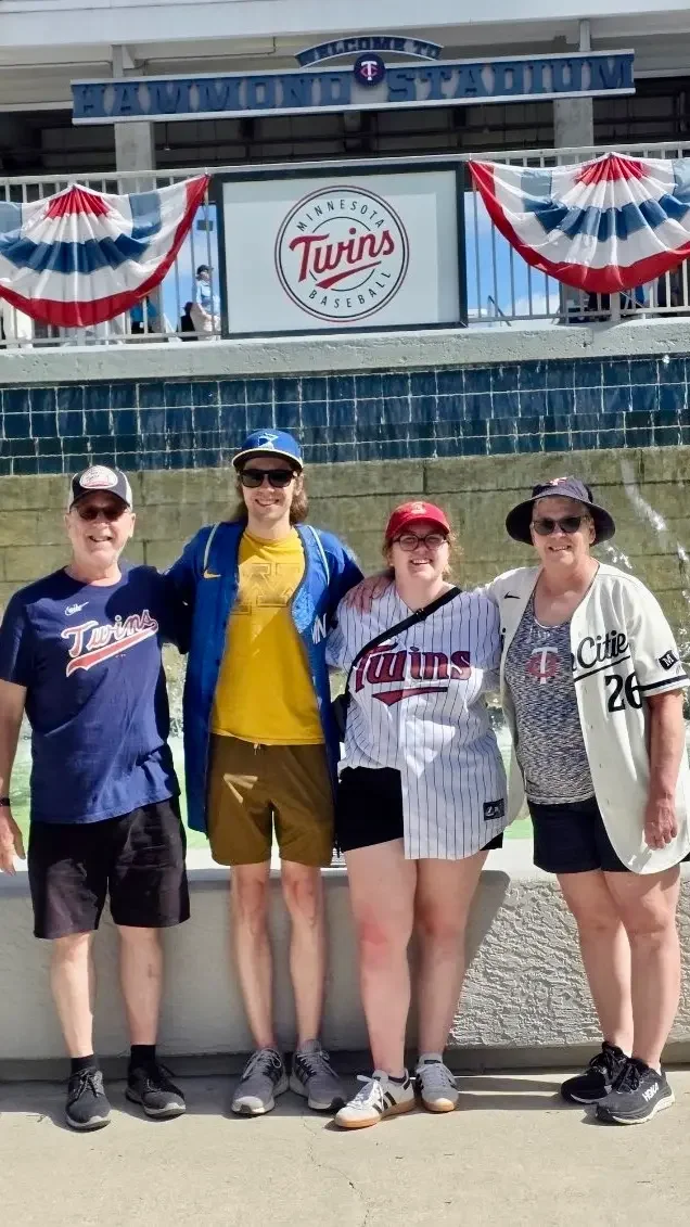 Four women standing in front of Target Field stadium, dressed in Twins baseball jerseys and casual clothing, smiling for the photo.