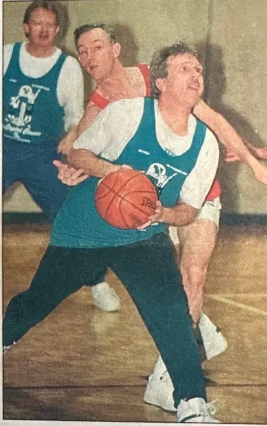 Three people playing basketball indoors, with the person in the foreground holding a basketball.