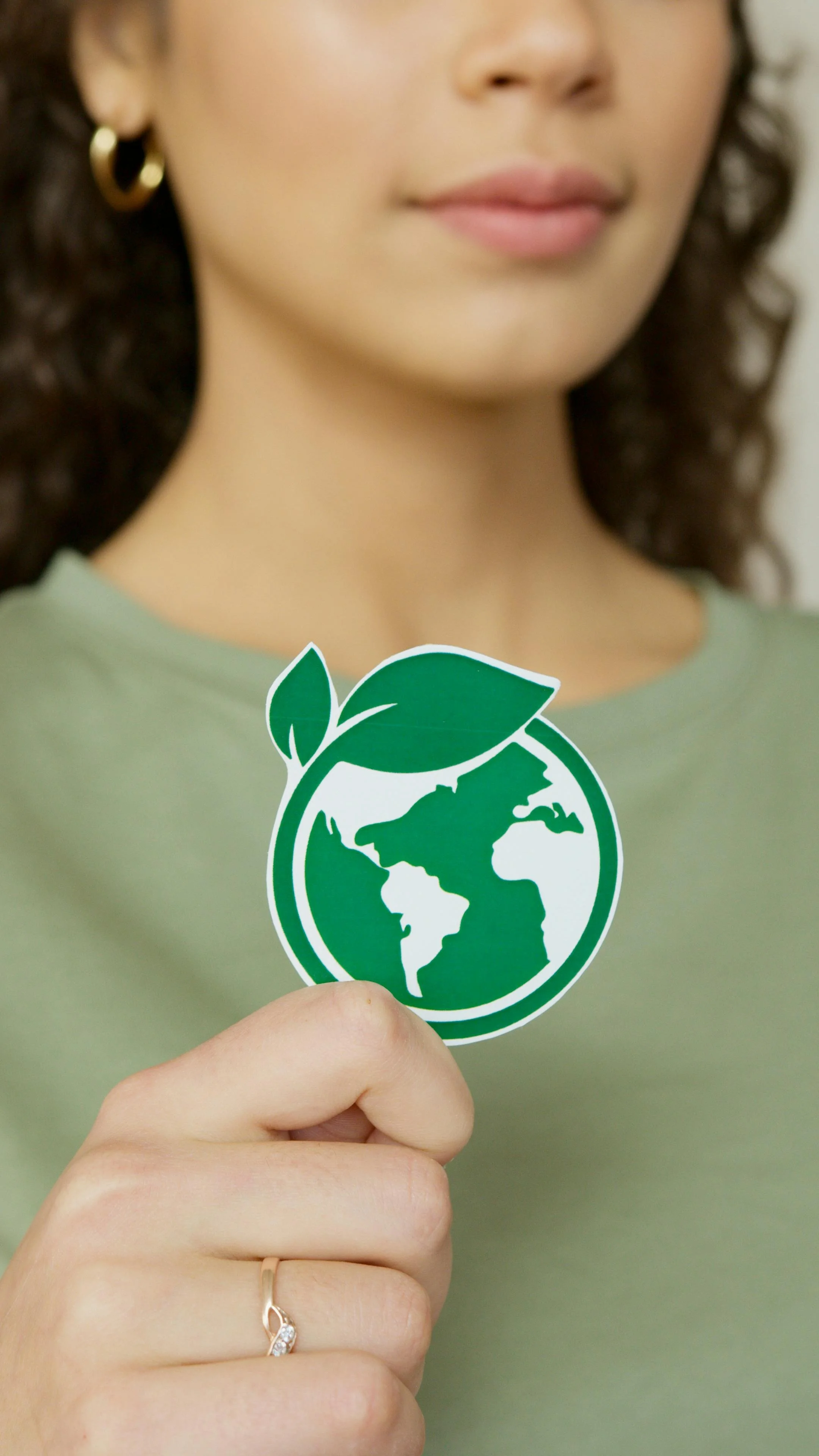 Close-up of a woman holding a sticker of the Earth with green leaves, symbolizing environmental awareness.